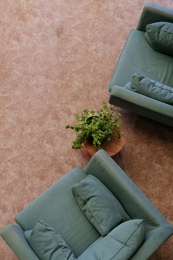Two sage green armchairs with cushions on a reddish-brown floor.