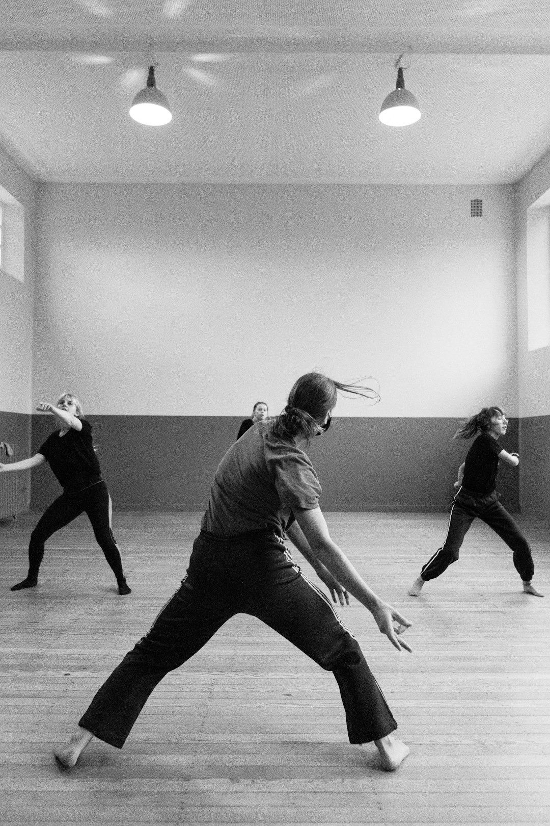 Four dancers in black and white mid-motion on a wooden floor.